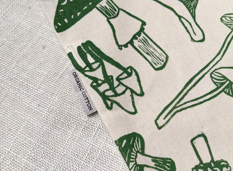 May include: A close-up of a white tote bag with a green mushroom print. The bag has a label that says "Organic Cotton".