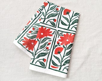 Peut inclure: Une serviette de cuisine blanche avec un imprimé floral rouge et vert. Le motif représente des fleurs et des feuilles stylisées dans un motif répétitif.