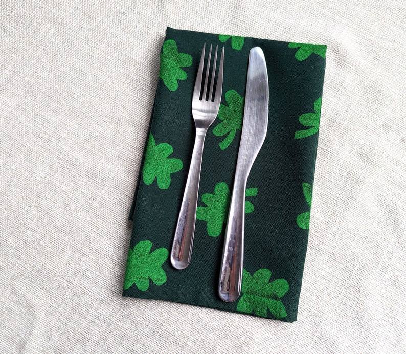 Puede incluir: Una servilleta de tela verde con estampado de tr&eacute;bol con un tenedor y un cuchillo de plata colocados encima.