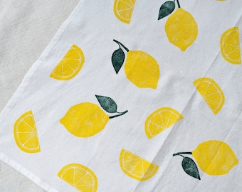 Peut inclure: Serviette de cuisine blanche avec un motif répété de citrons jaunes et de feuilles vertes. Les citrons sont imprimés dans un style d'impression en bloc.
