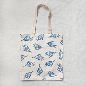 May include: A white tote bag with blue floral print. The bag has two long straps.