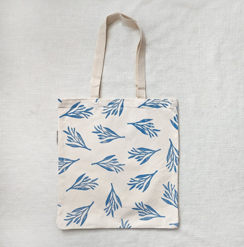 May include: A white tote bag with blue floral print. The bag has two long straps.
