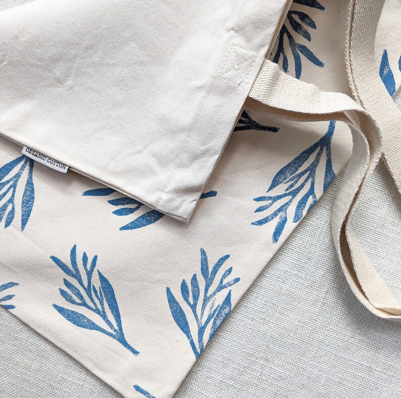 May include: A white tote bag with blue floral print and the words "Organic Cotton" on the front. The bag has two long straps.