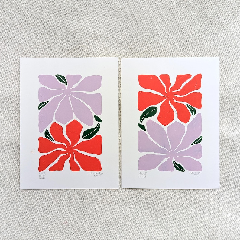 May include: Two prints of stylized floral designs. The first print features a purple flower on top of a red flower. The second print features a red flower on top of a purple flower. Both prints have green leaves.