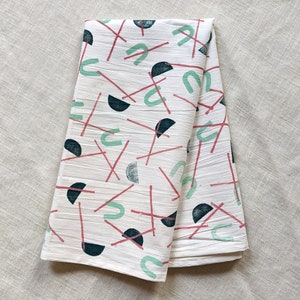May include: A white kitchen towel with a geometric pattern of red lines, green arcs, and black semi-circles.