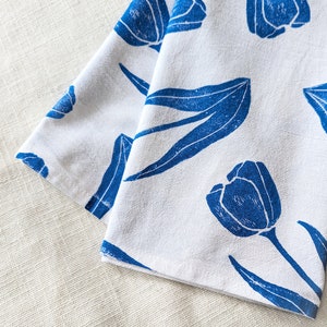 May include: A white cotton tea towel with a blue floral pattern. The pattern features stylized tulips and leaves.
