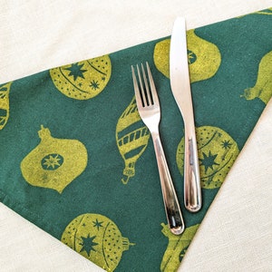 May include: A green fabric napkin with a gold Christmas ornament pattern. A silver fork and knife are placed on top of the napkin.