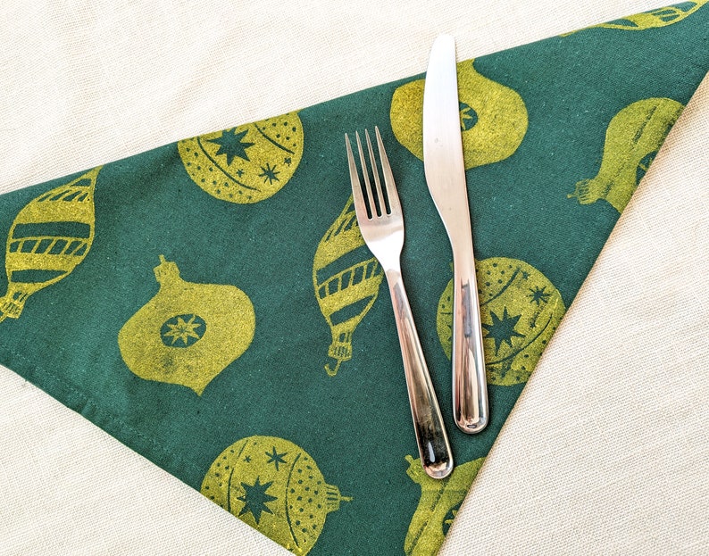 May include: A green fabric napkin with a gold Christmas ornament pattern. A silver fork and knife are placed on top of the napkin.