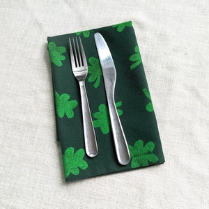 Puede incluir: Una servilleta de tela verde con estampado de tr&eacute;bol con un tenedor y un cuchillo de plata colocados encima.