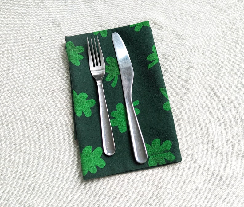 Puede incluir: Una servilleta de tela verde con estampado de tr&eacute;bol con un tenedor y un cuchillo de plata colocados encima.