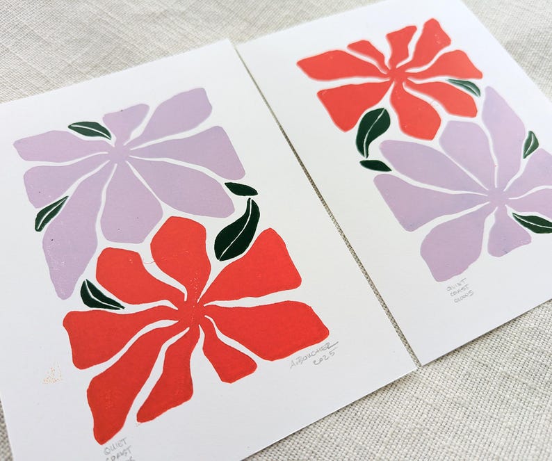 May include: Two floral prints with a purple and red flower design. The prints are on white paper and have a handwritten signature in the bottom right corner.