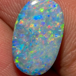 May include: An oval-shaped opal gemstone featuring a translucent white base with vibrant flashes of blue, green, and red color play throughout the stone. The surface is smooth and polished, reflecting light across its multifaceted internal structure.