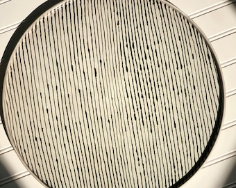 May include: A white ceramic serving tray with black vertical lines and black dots. The tray is round and has a slightly raised rim.