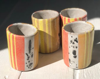 May include: Four ceramic mugs with yellow, orange, and white striped patterns. The mugs have a speckled glaze and some have black speckles.