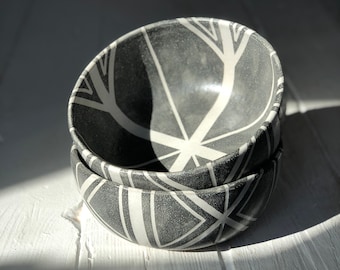 May include: Two black ceramic bowls with a white geometric pattern. The bowls are stacked on top of each other.