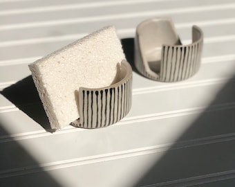 May include: Two ceramic sponge holders with black and white striped designs. One holder has a sponge inside.