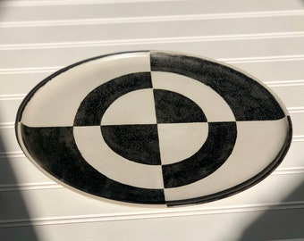May include: A white ceramic plate with a black and white checkered pattern. The plate has a slightly raised rim and a glossy finish.