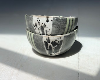 May include: Two stacked ceramic bowls with a black and white speckled glaze and green stripes.