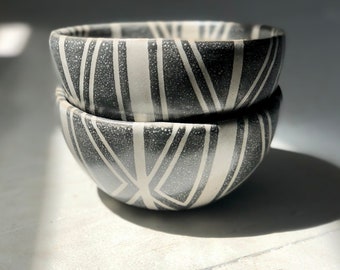 May include: Two black and white ceramic bowls with a geometric pattern. The bowls are stacked on top of each other.