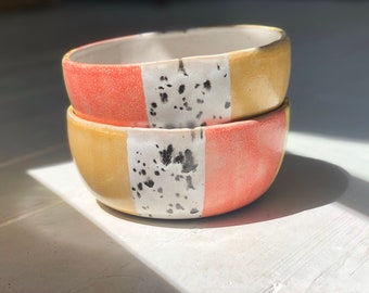 May include: Two stacked ceramic bowls with a speckled glaze. The bowls are yellow, orange, and white with black speckles.
