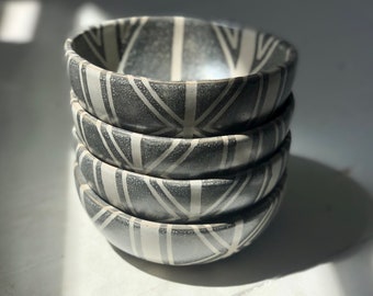 May include: A stack of four small ceramic bowls with a black and white geometric pattern. The bowls are stacked on a white surface.