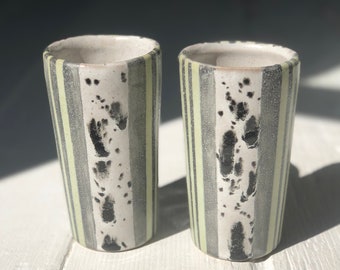 May include: Two ceramic cups with a striped pattern in black, white, and light green. The cups have a speckled glaze and a slightly textured surface.