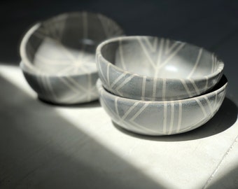 May include: Three gray ceramic bowls with white geometric patterns. The bowls are stacked on top of each other.