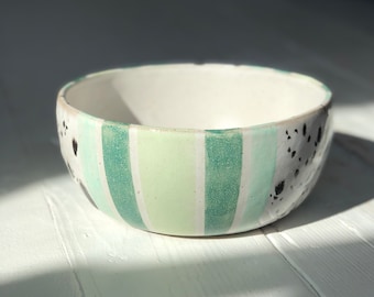 May include: A white ceramic bowl with a green and white striped pattern and black speckles.