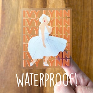 May include: A clear sticker featuring a cartoon illustration of a woman in a white dress, with the text "IVY LYNN" repeated in an orange pattern. The word "WATERPROOF!" is written in white below the image.
