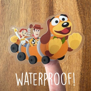 May include: A waterproof sticker featuring Toy Story characters Woody, Jessie, and Slinky Dog riding in a wagon. The sticker is on a finger and the text "WATERPROOF!" is below the sticker.