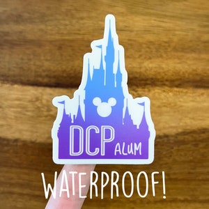 May include: A purple and blue sticker with a silhouette of Cinderella's castle and the text "DCP ALUM" inside. The sticker is waterproof.