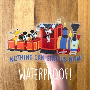 May include: A clear sticker featuring Mickey Mouse, Minnie Mouse, Goofy, Pluto, and Donald Duck on a colorful train. The sticker has the text "NOTHING CAN STOP US NOW!" and "WATERPROOF!"
