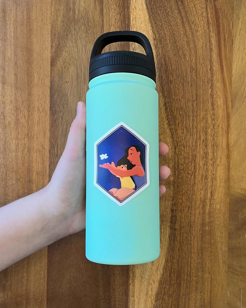 K&ouml;nnte beinhalten: Eine t&uuml;rkisfarbene Wasserflasche mit schwarzem Deckel und Griff. Auf der Flasche befindet sich ein Aufkleber mit einer Frau und einem Kind mit einem Schmetterling.
