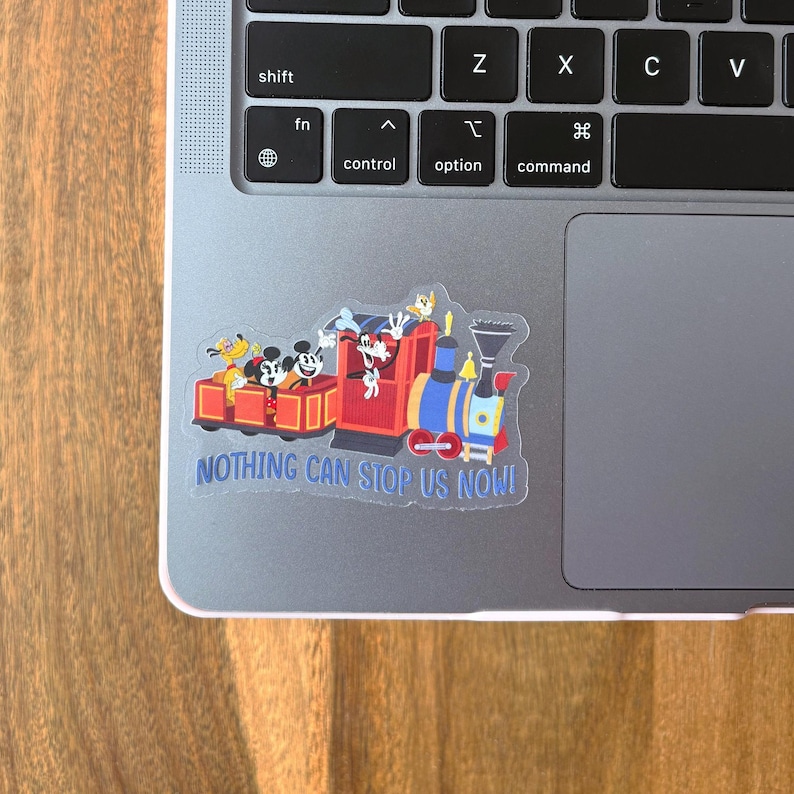May include: A colorful sticker featuring a cartoon train with Mickey Mouse, Donald Duck, and Goofy. The train is red, blue, and yellow, with the text "NOTHING CAN STOP US NOW!" on the bottom. The sticker is on a laptop.
