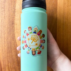 May include: A light teal water bottle with a black handle and lid. The bottle features a colorful sticker with cartoon figures around a sun with the text "it's a small world".