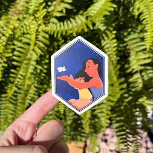 K&ouml;nnte beinhalten: Ein sechseckiger Aufkleber mit blauem Hintergrund und wei&szlig;en Sternen. Der Aufkleber zeigt ein Cartoon-Bild von zwei Frauen, eine mit langen schwarzen Haaren und die andere mit kurzen schwarzen Haaren, die zu einem wei&szlig;en Schmetterling aufblicken.