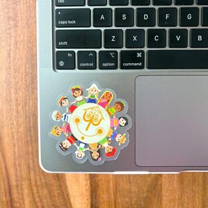 May include: A colorful sticker featuring a circular design with a central image of a building and the number 70. The sticker is surrounded by cartoon figures of children of different ethnicities. The sticker is placed on a laptop.