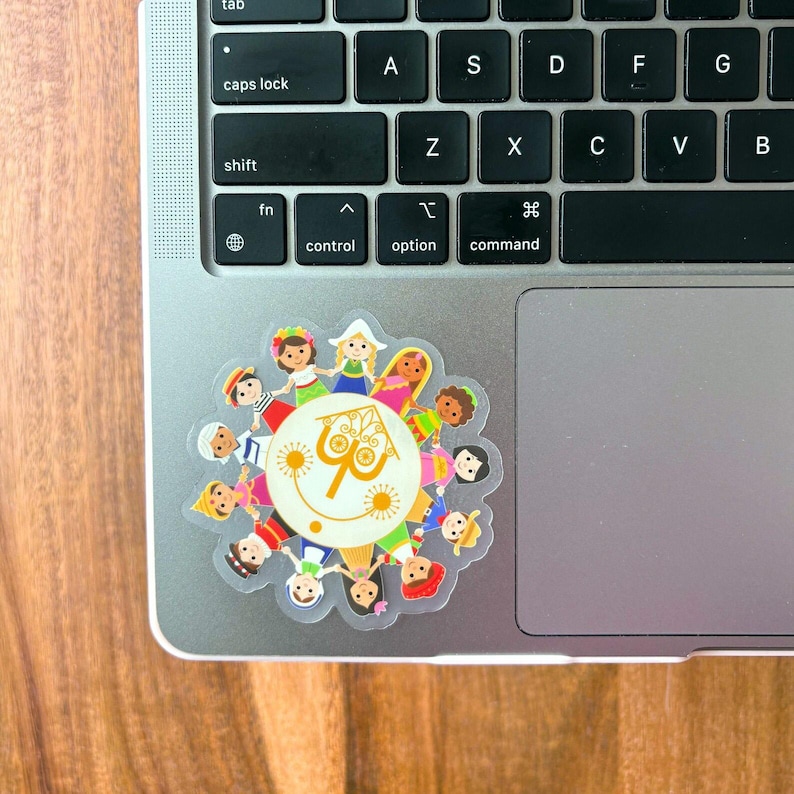 May include: A colorful sticker featuring a circular design with a central image of a building and the number 70. The sticker is surrounded by cartoon figures of children of different ethnicities. The sticker is placed on a laptop.