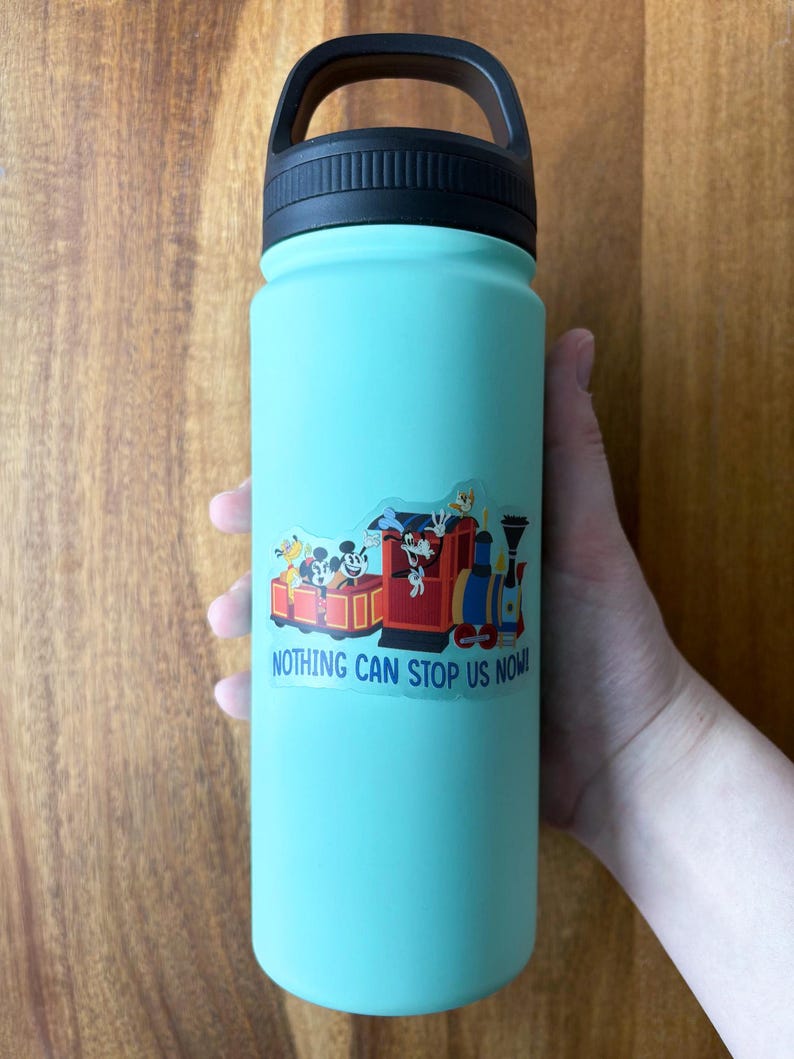 May include: A teal water bottle with a black handle and lid. A colorful sticker featuring cartoon characters on a train with the text "NOTHING CAN STOP US NOW!" is affixed to the bottle.