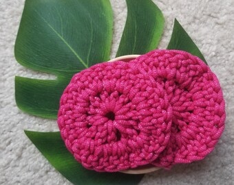 Puede incluir: Tres almohadillas de maquillaje de crochet rosa en un tazón. Las almohadillas están hechas con un hilo brillante.
