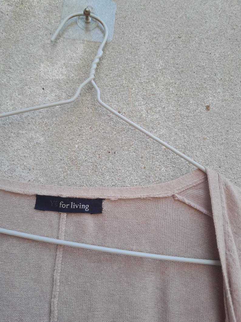 K&ouml;nnte beinhalten: Hellbeige Cardigan an einem wei&szlig;en Metallb&uuml;gel. Das Etikett zeigt "Y's for living" in wei&szlig;er Schrift auf schwarzem Hintergrund. Der Cardigan ist aus weichem Strickmaterial gefertigt.