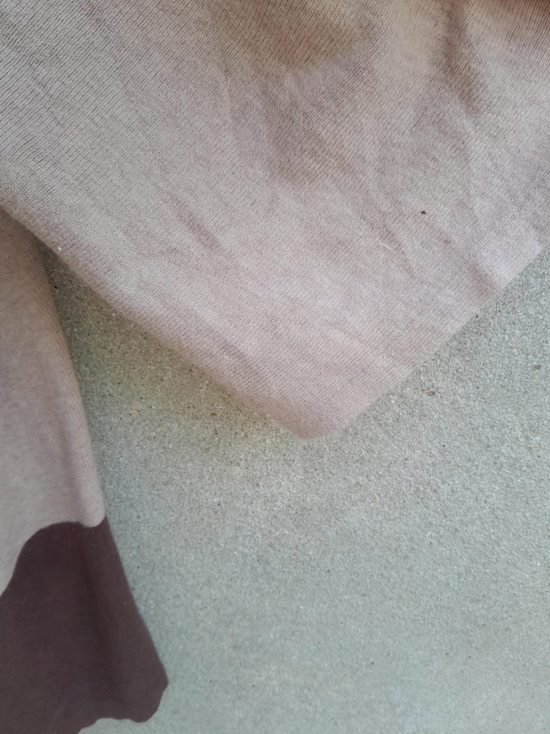 K&ouml;nnte beinhalten: Nahaufnahme eines beigen und braunen Stoffes. Der Stoff scheint ein weiches Strickmaterial zu sein, mit einem dunkleren braunen Abschnitt am unteren Rand. Der Hintergrund ist eine strukturierte, hellgraue Oberfl&auml;che.