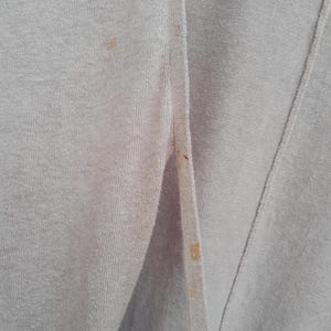 K&ouml;nnte beinhalten: Nahaufnahme eines hellvioletten Cardigans mit sichtbaren Flecken. Der Cardigan hat eine Knopfleiste vorne und eine gerippte Textur. Der Stoff scheint ein weiches Strickmaterial zu sein. Das Bild zeigt die Vorderseite des Kleidungsst&uuml;cks.