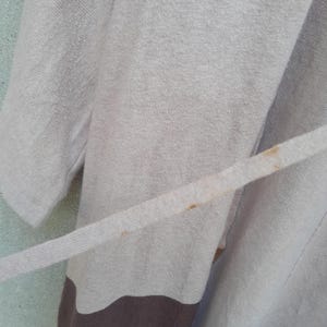 K&ouml;nnte beinhalten: Ein hellbeige Robe mit passendem G&uuml;rtel. Die Robe hat unten einen braunen Einsatz und einen hellblauen Hintergrund. Der Stoff scheint weich und strukturiert zu sein.