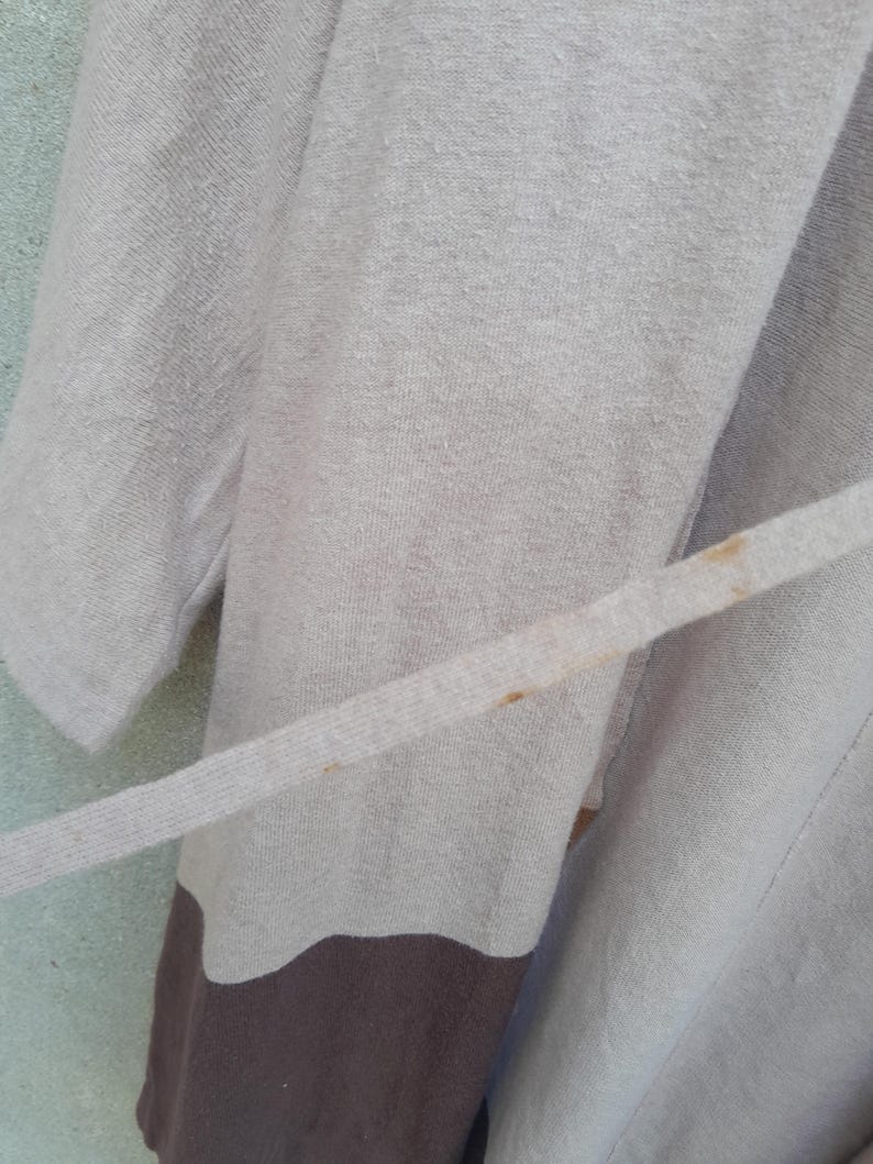 K&ouml;nnte beinhalten: Ein hellbeige Robe mit passendem G&uuml;rtel. Die Robe hat unten einen braunen Einsatz und einen hellblauen Hintergrund. Der Stoff scheint weich und strukturiert zu sein.