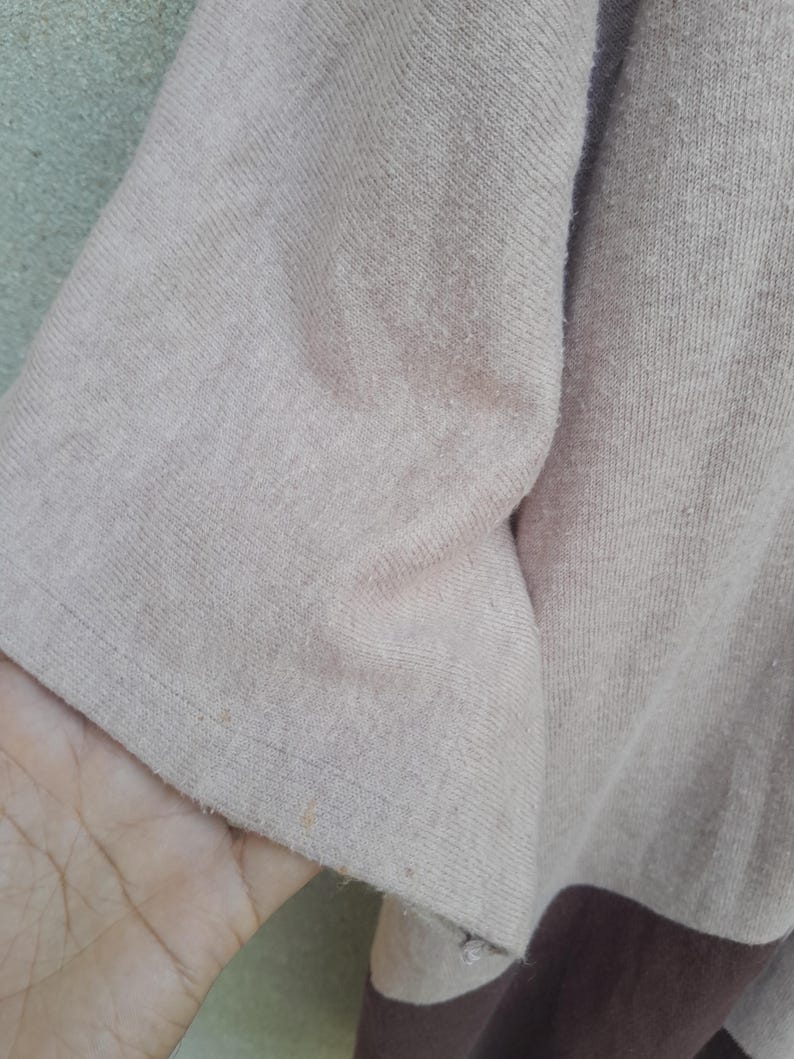 K&ouml;nnte beinhalten: Nahaufnahme eines hellbraunen Kurzarmshirts. Der &Auml;rmel ist sichtbar, mit einem braunen Streifen am unteren Rand. Der Stoff scheint ein weiches Strickmaterial zu sein.
