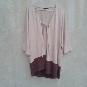 K&ouml;nnte beinhalten: Ein beige-brauner Cardigan mit Farbblock-Design, V-Ausschnitt und Dreiviertel&auml;rmeln h&auml;ngt an einem Metallb&uuml;gel. Der obere Teil ist beige, der untere Teil ist dunkelbraun. Der Cardigan hat einen Bindverschluss und Holzkn&ouml;pfe.