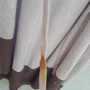 K&ouml;nnte beinhalten: Ein beigefarbener und brauner Kapuzenpullover mit Kordelzug. Der Pullover hat ein Farbblock-Design mit einem braunen unteren Bereich und einem beigen oberen Bereich. Der Kordelzug ist beige mit einem braunen Fleck.