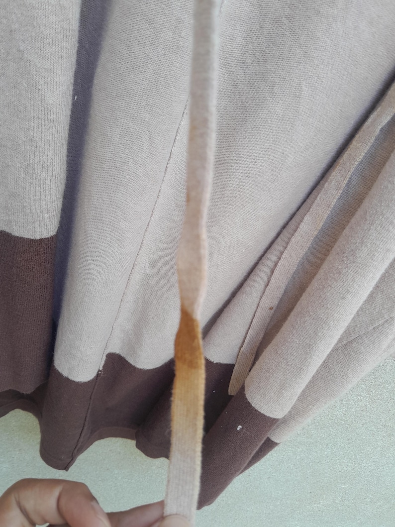 K&ouml;nnte beinhalten: Ein beigefarbener und brauner Kapuzenpullover mit Kordelzug. Der Pullover hat ein Farbblock-Design mit einem braunen unteren Bereich und einem beigen oberen Bereich. Der Kordelzug ist beige mit einem braunen Fleck.