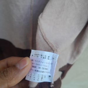 K&ouml;nnte beinhalten: Beige-braunes Kleidungsst&uuml;ck mit einem Etikett mit der Aufschrift "MADE IN CHINA". Das Etikett enth&auml;lt auch japanischen Text und eine Telefonnummer. Das Kleidungsst&uuml;ck hat ein zweifarbiges Design.